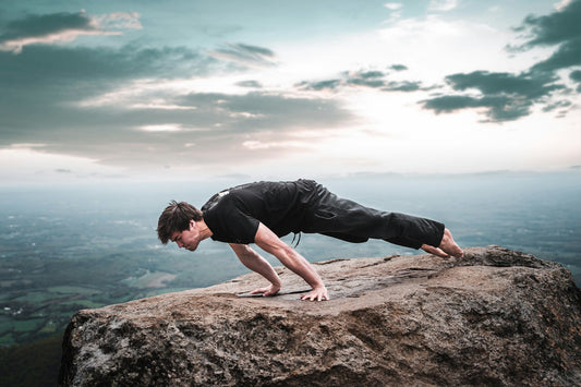 Athlete holding a planche on a rock above the sea